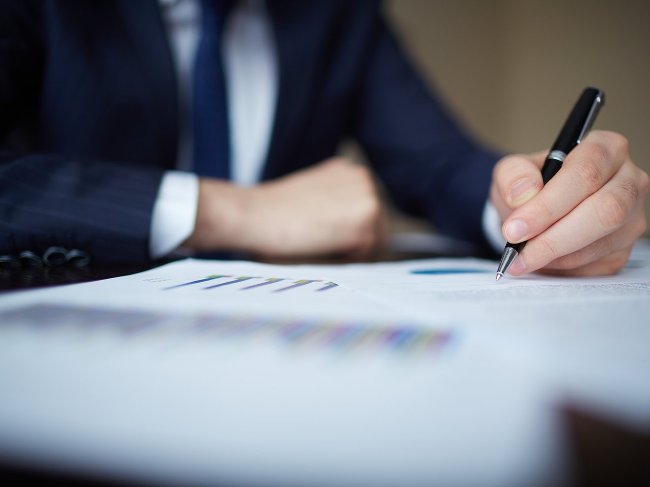 Image of human hand with pen over documents at workplace